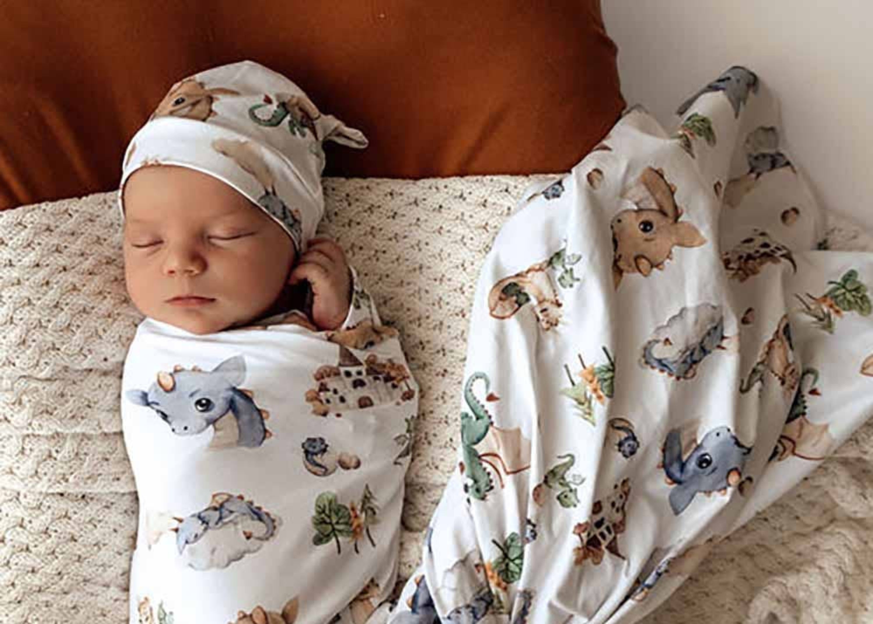 Newborn baby swaddled in a blanket with animal patterns on a brown surface.